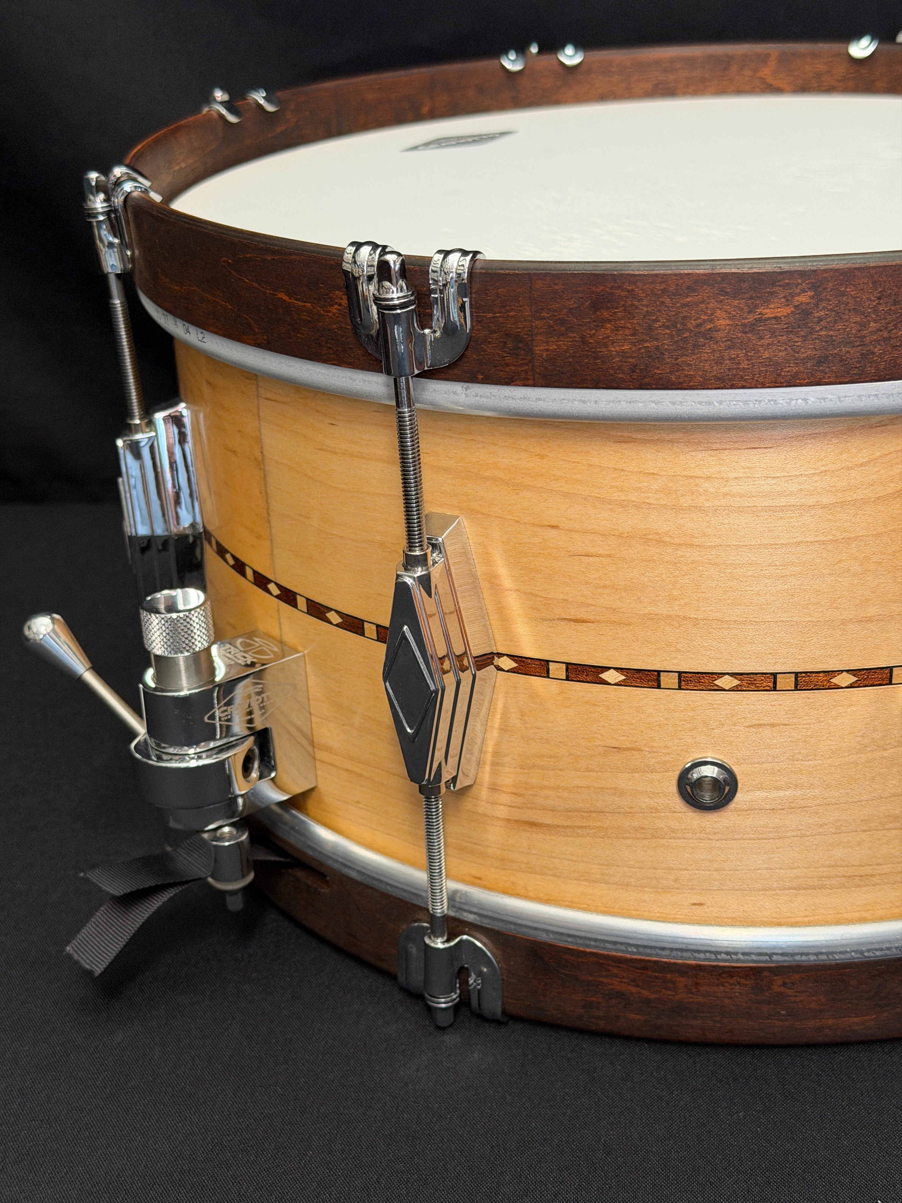 Close-up of a banjo with a focus on the head and tuning pegs against a dark background.